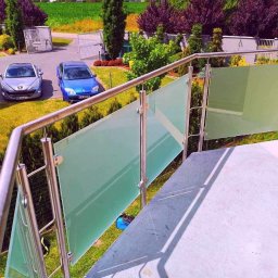 Prosto z projektu Kamil Gąsiorowski - Szklana balustrada z nierdzewną poręczą na schodach zewnętrznych, w tle dwa samochody i brama wjazdowa.