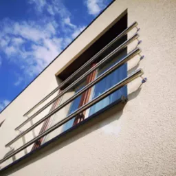 Nowoczesna, minimalistyczna balustrada okienna ze stali nierdzewnej, zamontowana na elewacji budynku. Widok pod kątem, błękitne niebo w tle.