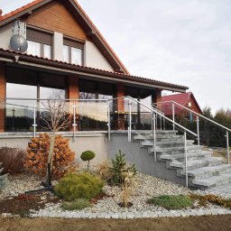 Prosto z projektu Kamil Gąsiorowski - Nowoczesna szklana balustrada z metalowymi poręczami, otaczająca taras domu z cegły, z kamiennymi schodami i ozdobnym ogrodem na pierwszym planie.