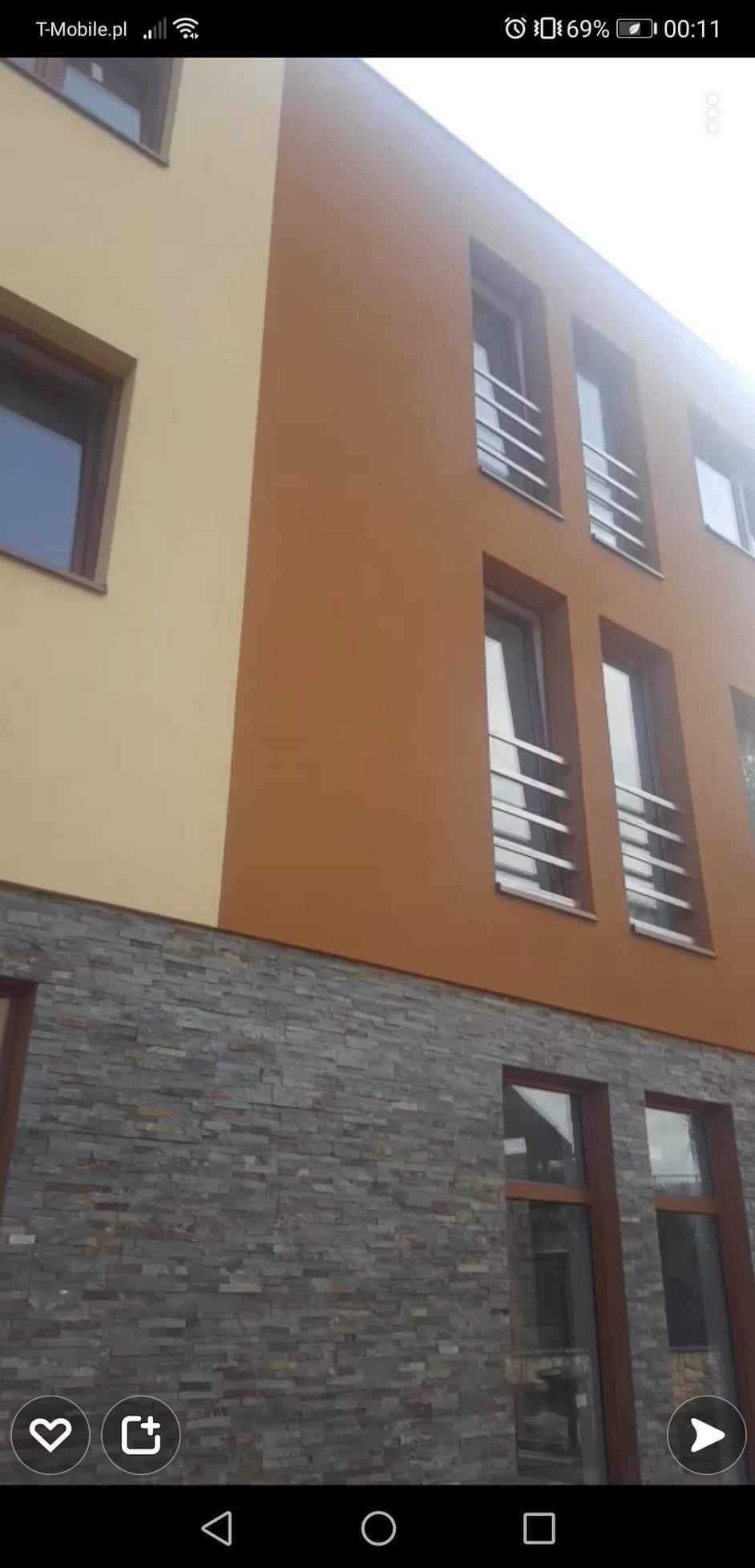 Elewacja budynku z kamienną okładziną i stalowymi balustradami okiennymi. Ujęcie z dołu, podkreślające nowoczesny design i połączenie kolorów.