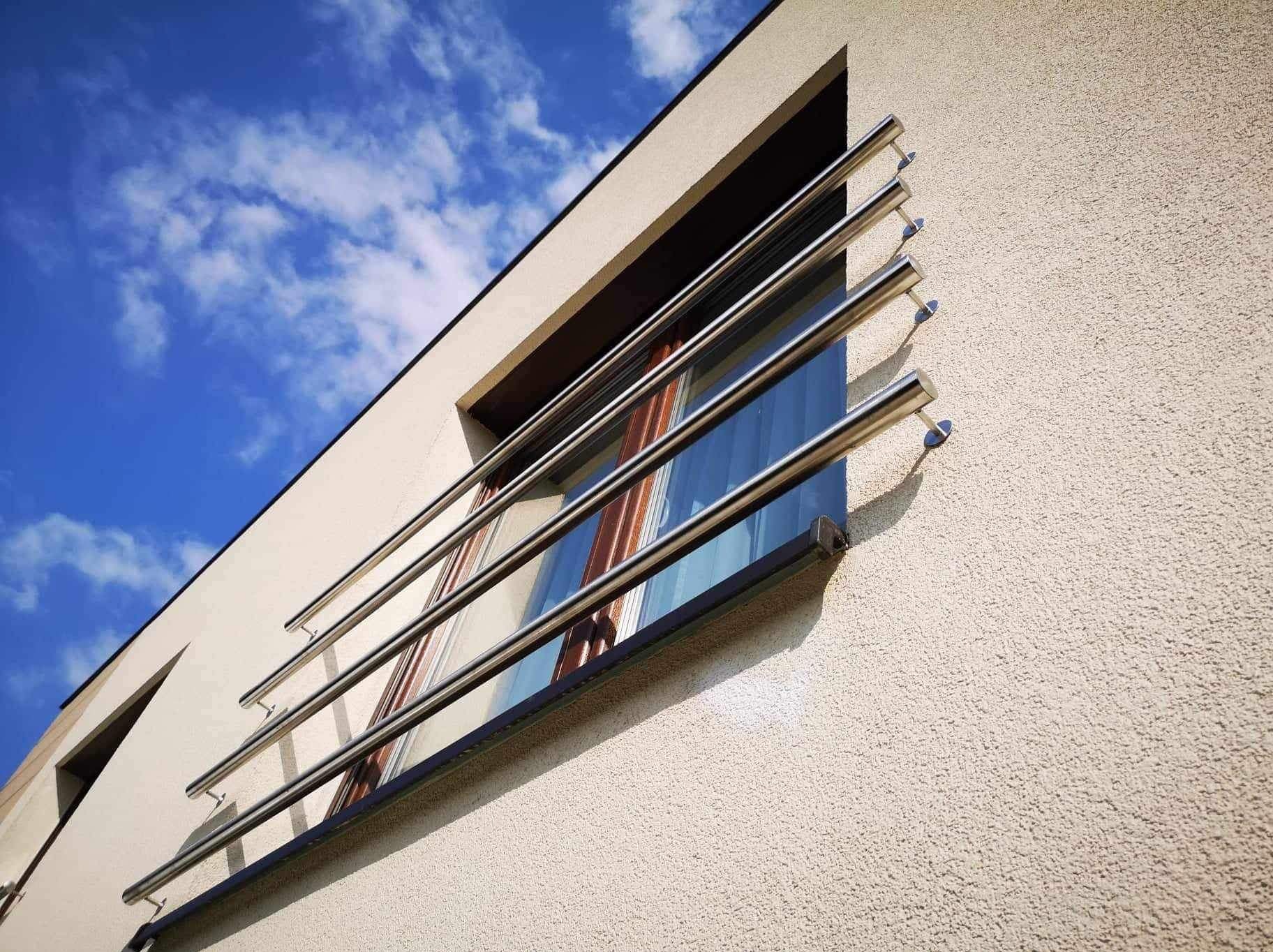 Nowoczesna, minimalistyczna balustrada okienna ze stali nierdzewnej, zamontowana na elewacji budynku. Widok pod kątem, błękitne niebo w tle.
