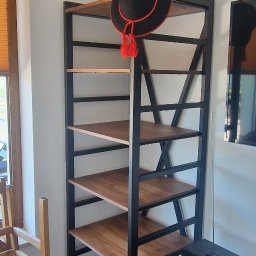 PMP-TECH - Regał metalowy z drewnianymi półkami w stylu industrialnym, ozdobiony czarnym kapeluszem z czerwonymi pomponami. Widok z boku, jasne wnętrze, fragment krzesła.