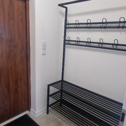 PMP-TECH - Nowoczesny, czarny metalowy wieszak na ubrania i buty w przedpokoju z brązowymi drzwiami, marmurową podłogą i białymi ścianami. Minimalistyczny design.