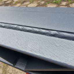 PMP-TECH - Szlifowana, spawana konstrukcja stalowa pomalowana na szaro, z widocznymi śladami spawania, leżąca na zewnątrz. Ukazana z bliska, pod kątem.