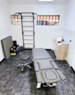 Nowoczesny gabinet rehabilitacyjny w Mysłowicach. Profesjonalny stół do masażu, drabinki gimnastyczne, krzesło obrotowe i szafka medyczna. Jasne wnętrze.