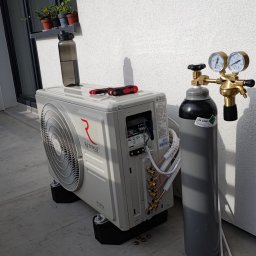 EcoPrecision Mateusz Mazur - Biała jednostka zewnętrzna klimatyzacji Rotenso Hiro Series, butla z gazem i narzędzia na betonowym podłożu przy ścianie z oknem i doniczkami.