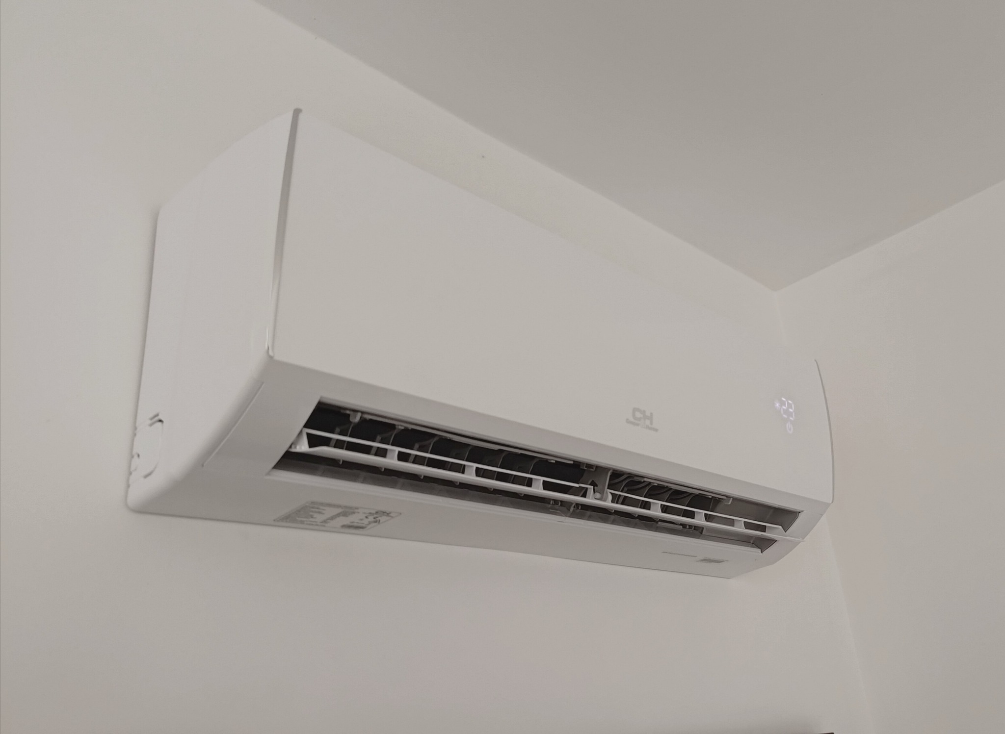Biała klimatyzacja marki CH zamontowana na ścianie w pomieszczeniu. Widoczny wyświetlacz temperatury i logo. Minimalistyczny design.