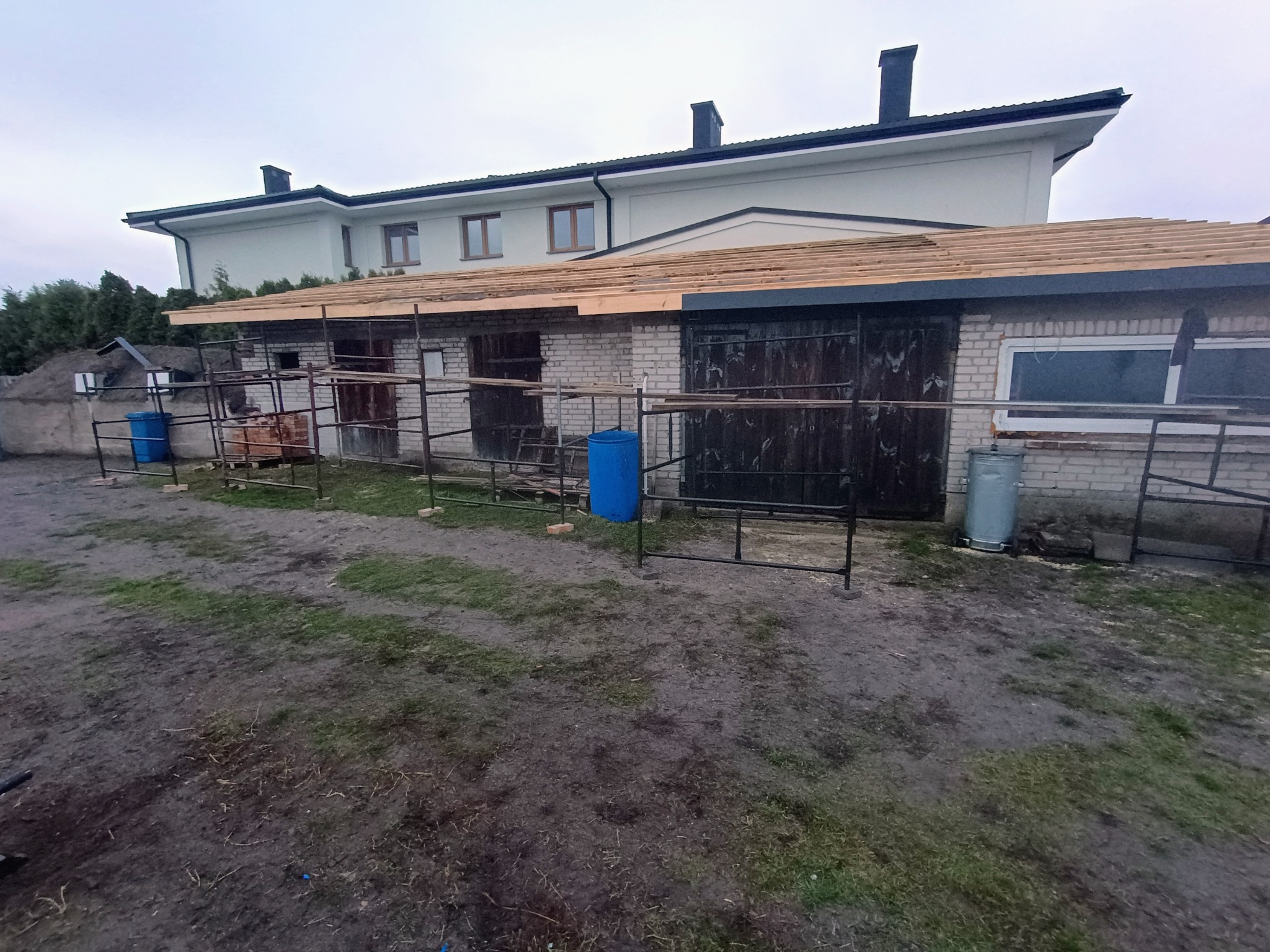 Konstrukcja dachu w trakcie budowy w Białej Podlaskiej. Widoczne drewniane elementy więźby i rusztowania. Budynek z białej cegły w tle.