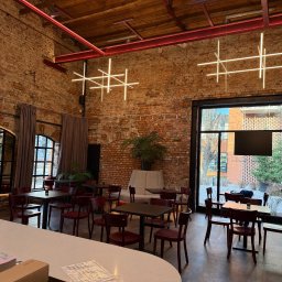 Elix Vitalii Kovalchuk - Wnętrze restauracji z ceglanymi ścianami i nowoczesnym oświetleniem w kształcie krzyży. Widoczne stoliki z krzesłami i duże okna z widokiem na zewnątrz.