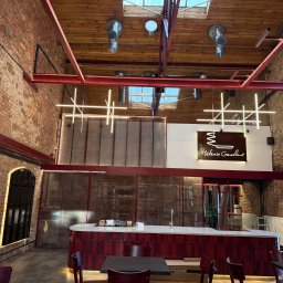 Elix Vitalii Kovalchuk - Loftowe wnętrze restauracji z ceglanymi ścianami i nowoczesnym oświetleniem w postaci geometrycznych lamp wiszących. Widoczne elementy instalacji pod sufitem.