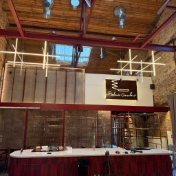 Elix Vitalii Kovalchuk - Nowoczesne oświetlenie LED w loftowym wnętrzu restauracji z ceglanymi ścianami i drewnianym stropem. Geometryczne lampy krzyżowe nad barem.