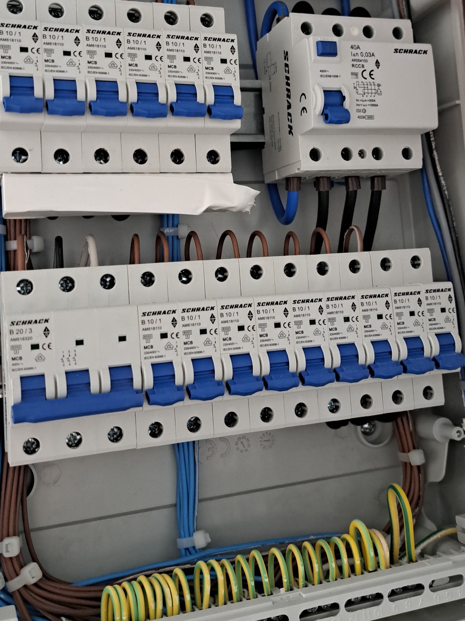 Rozdzielnica elektryczna Schrack z zainstalowanymi bezpiecznikami B10/1 i wyłącznikiem różnicowoprądowym 40A, widoczne kable w peszlach. Instalacja elektryczna.