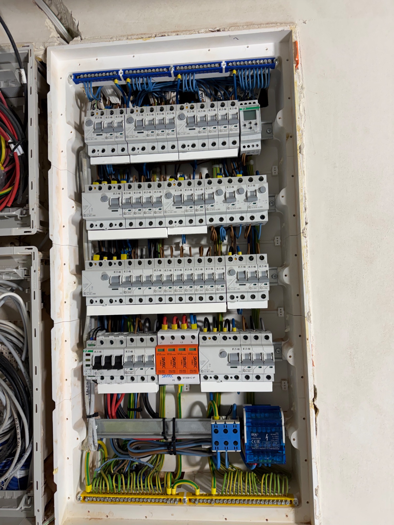 Rozdzielnica elektryczna z zainstalowanymi bezpiecznikami i okablowaniem, widok z bliska. Elementy marki Eaton i Simtec. Żółto-zielone przewody u dołu.