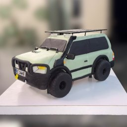 Ciacha by M - Tort w kształcie terenowego auta z bagażnikiem dachowym i tablicą rejestracyjną 'RZ DAWID', na białym podeście. Jasne tło.