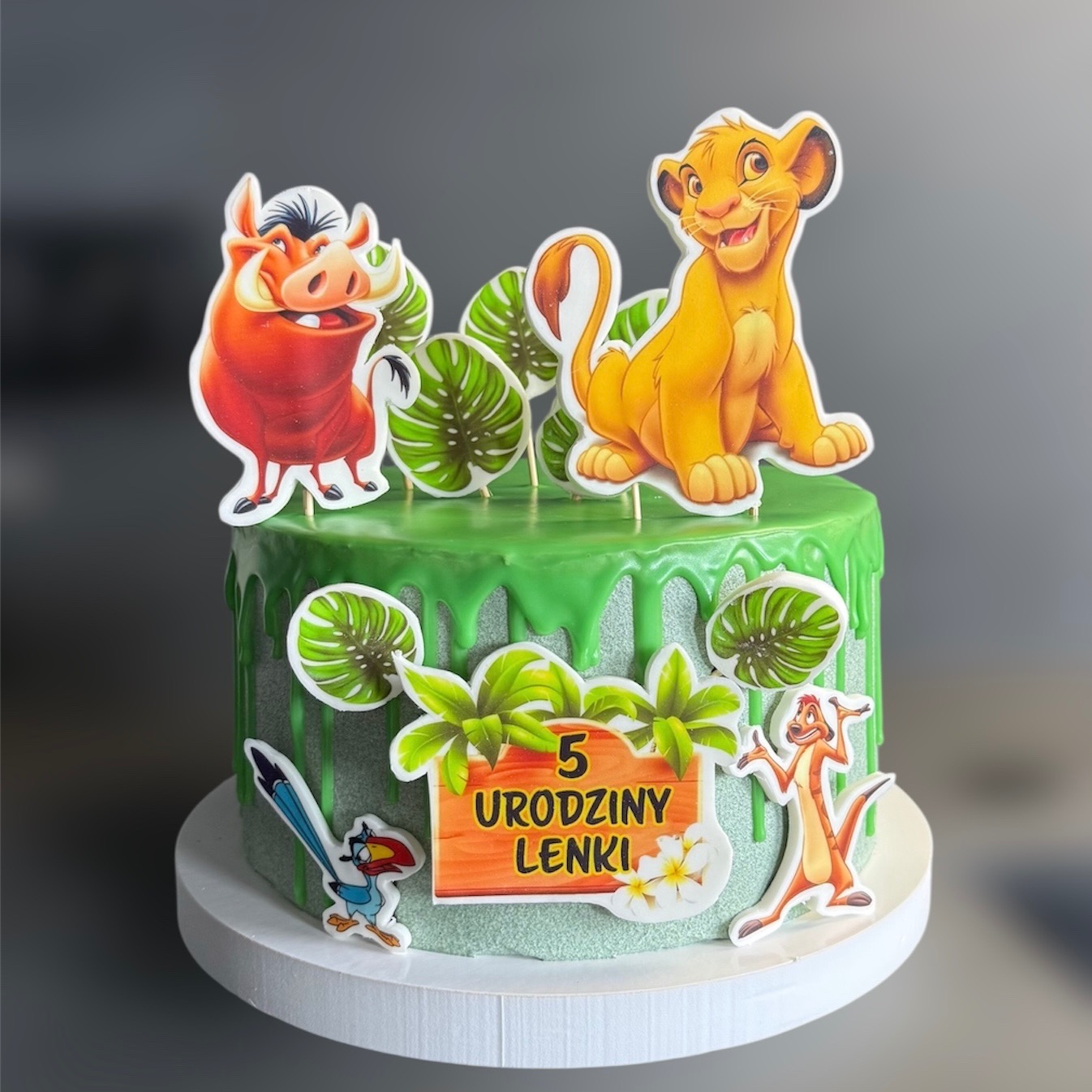 Tort urodzinowy z zielonym lukrem i postaciami z Króla Lwa, dekorowany motywami roślinnymi. Napis: 5 Urodziny Lenki.