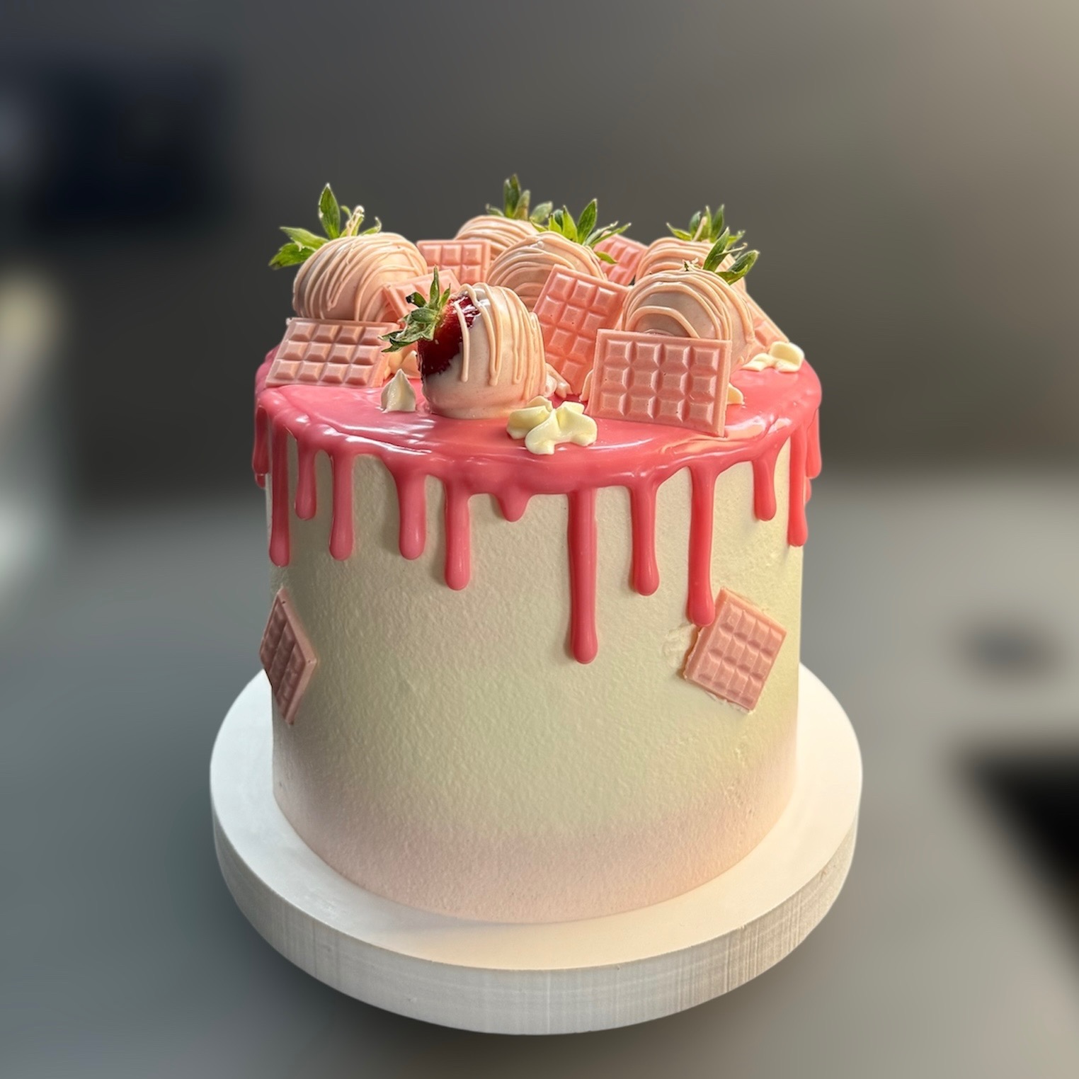 Różowy tort z truskawkami w polewie i czekoladkami, na białym podeście. Elegancki, nowoczesny design z dbałością o detale.