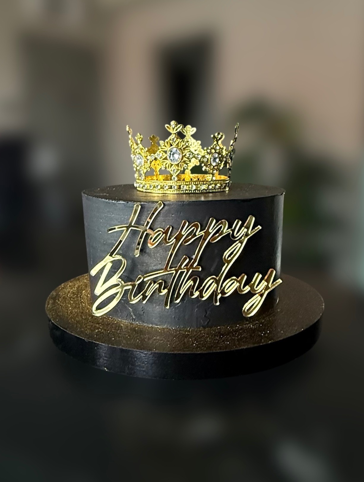 Czarny tort urodzinowy z koroną i złotym napisem 'Happy Birthday' na czarnym, błyszczącym podkładzie. Elegancki i stylowy.