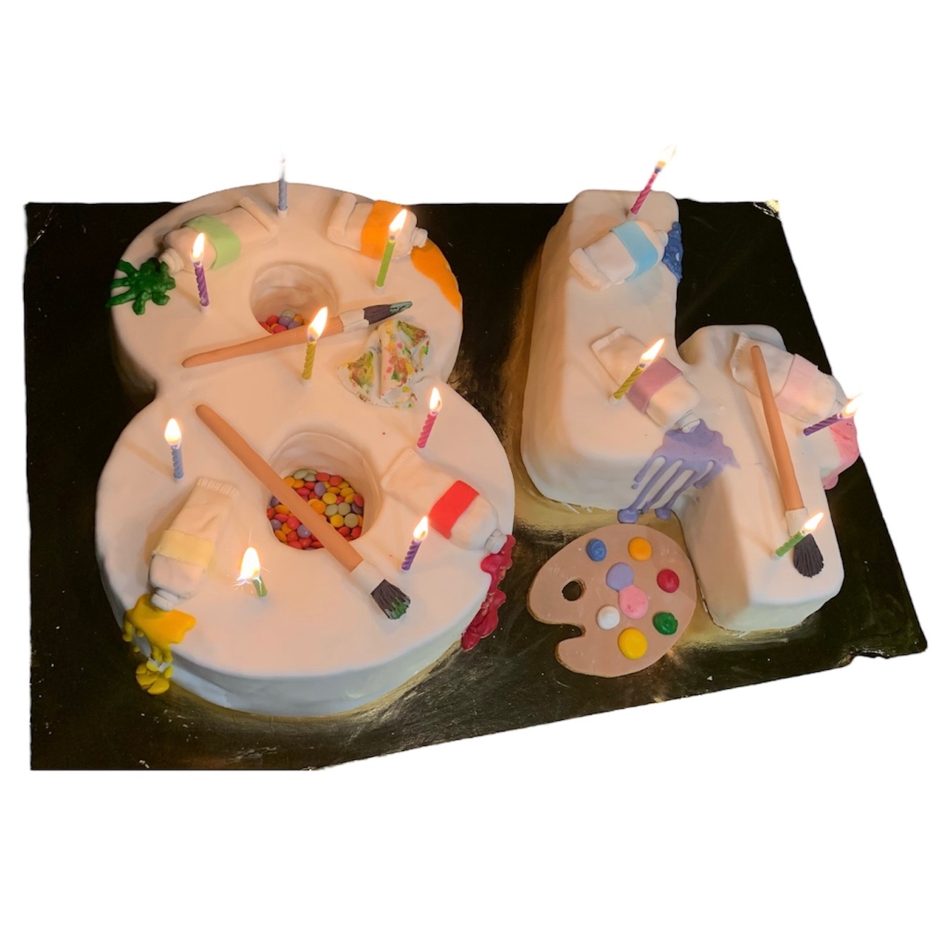 Tort urodzinowy w kształcie liczby 81 z motywem malarskim: farby, pędzle, paleta, świeczki. Unikalny wypiek z Rzeszowa na złotym podkładzie.