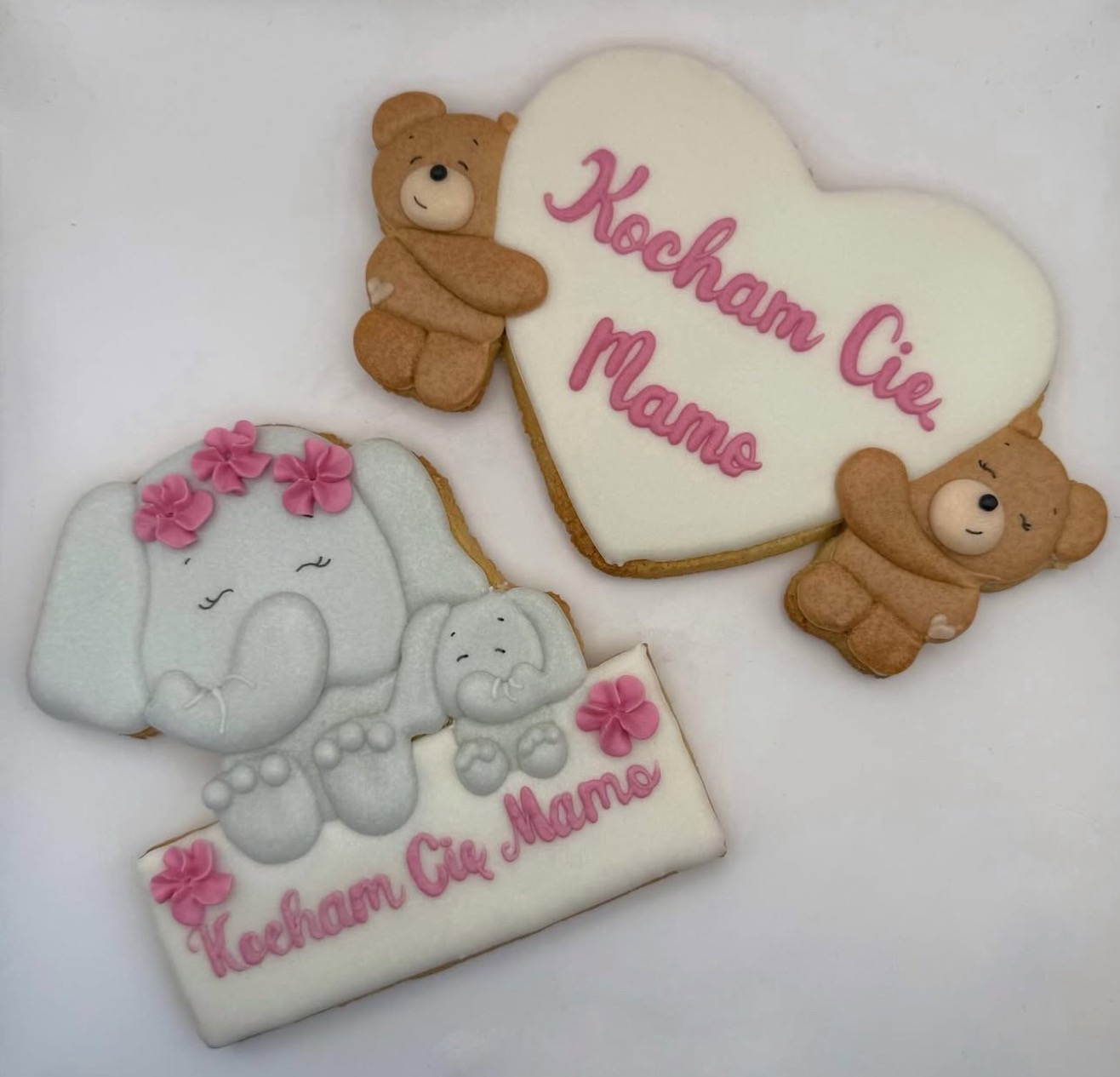 Ręcznie robione, lukrowane ciasteczka w kształcie słonia z kwiatami i serca z misiami, z napisem 'Kocham Cię Mamo', na białym tle.