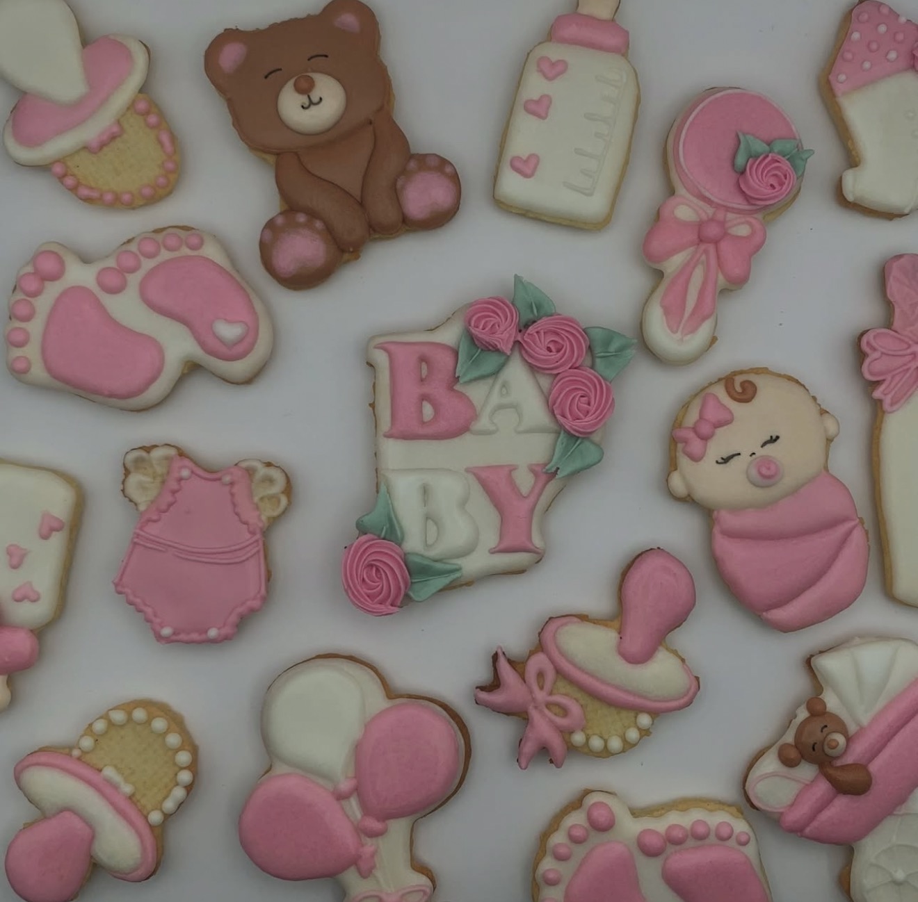 Ręcznie robione, urocze pierniczki w kształcie niemowlęcych akcesoriów (butelki, stópki, misie) z różowym lukrem, idealne na baby shower.