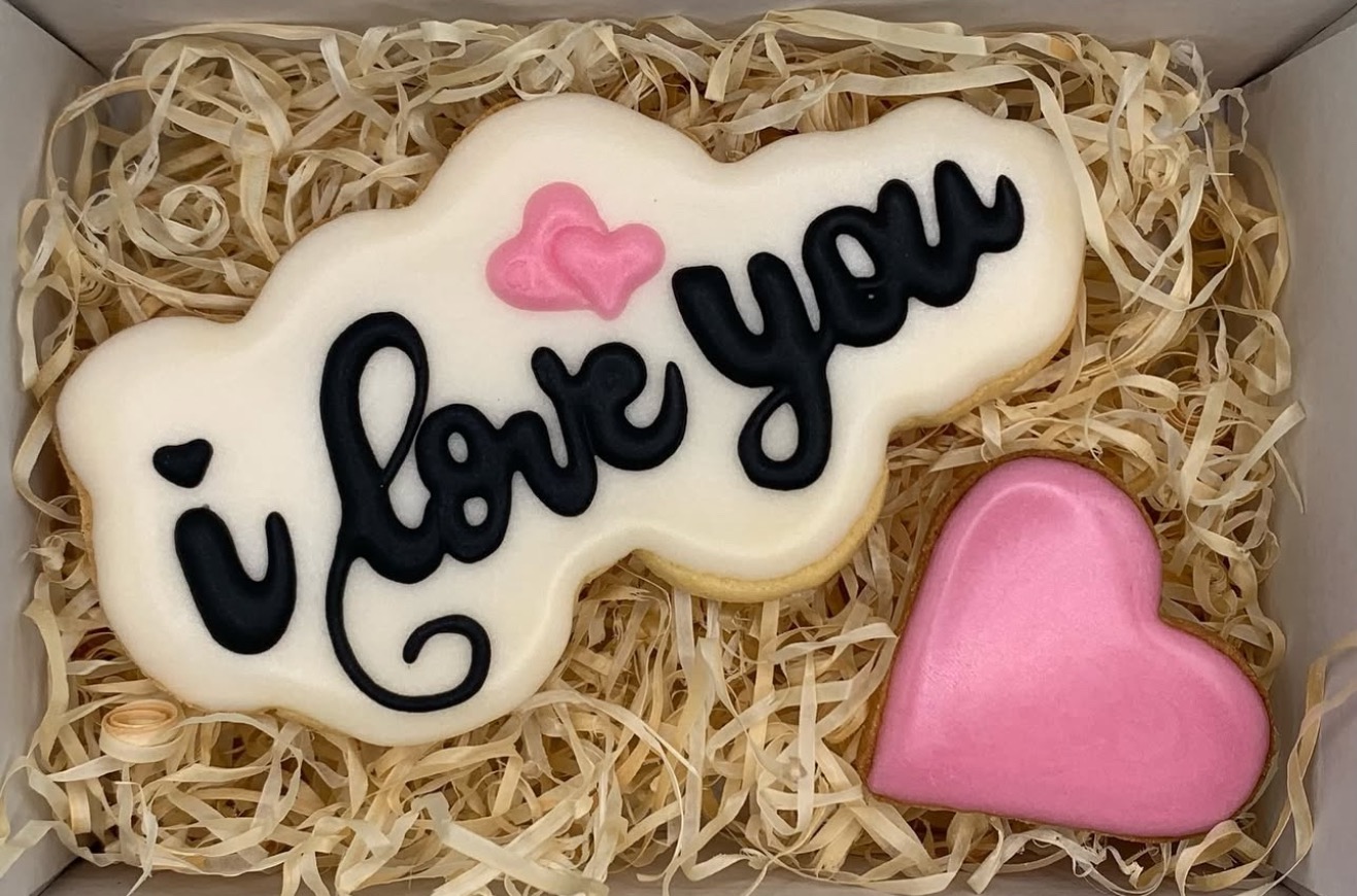Ręcznie robione ciasteczka w pudełku prezentowym: jedno w kształcie chmurki z napisem 'I love you' i dwa różowe serca, idealne na Walentynki.