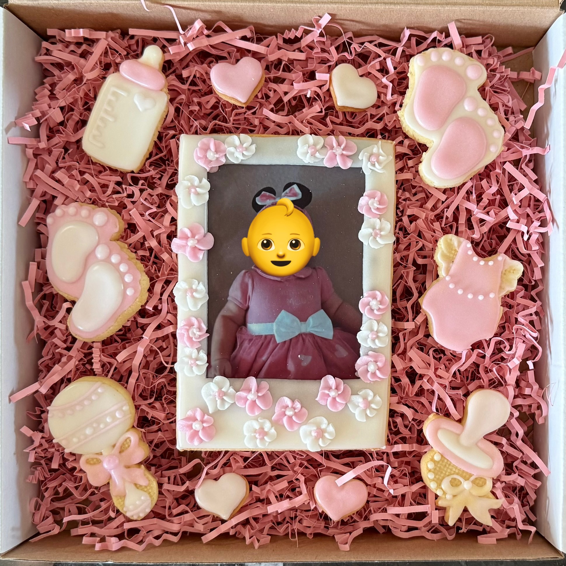 Ręcznie robione ciasteczka w kształcie niemowlęcych atrybutów (butelka, stópki, grzechotka) i serduszek, otaczające jadalną ramkę z niemowlęcym zdjęciem w pudełku.