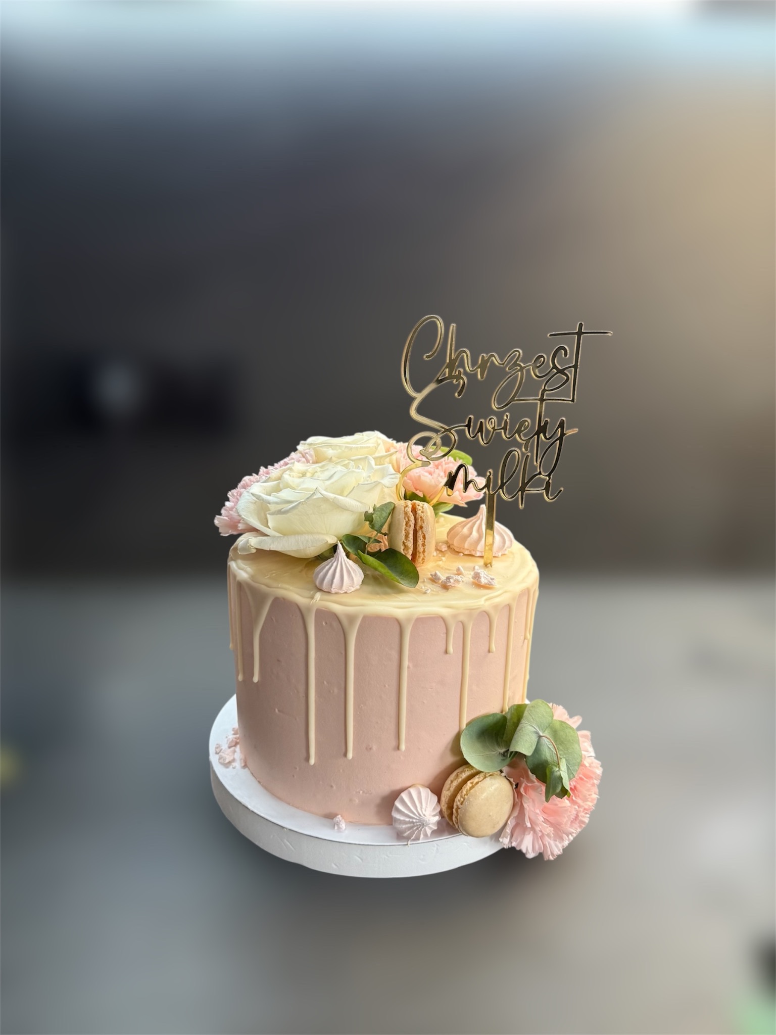 Tort na chrzest z białymi różami, makaronikami i złotym topperem 'Chrzest Święty Milki'. Różowy krem ocieka białą polewą. Elegancki i delikatny.