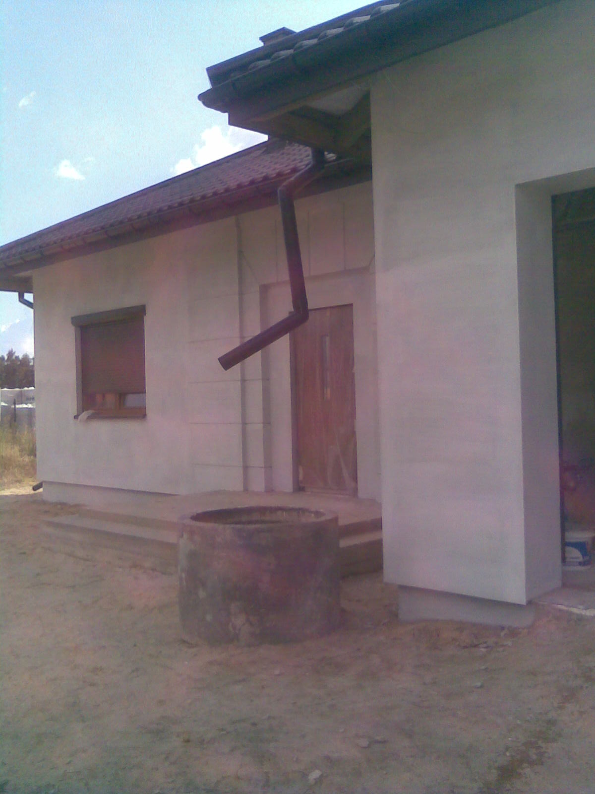 Surowy budynek jednorodzinny w Piotrków Tryb. z nową elewacją i rynną, widoczny stary betonowy krąg na podwórku.