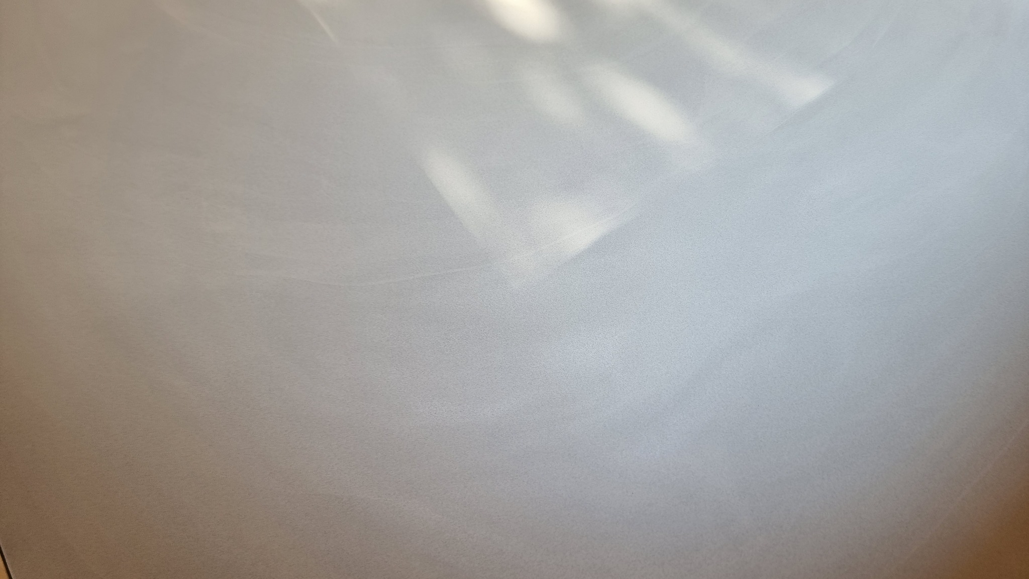 Jasnoszara, gładka posadzka z delikatnym połyskiem, oświetlona naturalnym światłem słonecznym wpadającym przez okno, tworzącym subtelne refleksy.