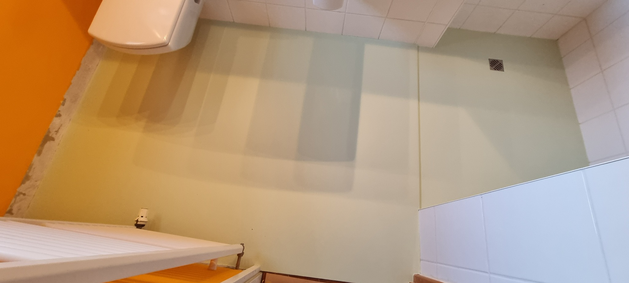 Fragment łazienki z umywalką, częściowo wykończoną ścianą w odcieniach żółci i białymi płytkami. Widoczny fragment grzejnika drabinkowego.