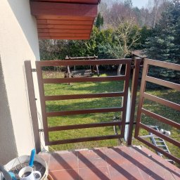 MONISTAL Jakub Janowski - Balkon z brązową, metalową balustradą o nowoczesnym designie. Na pierwszym planie donica z kwiatami i kubek. W tle trawnik i drzewa. Widok z góry.