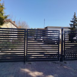 MONISTAL Jakub Janowski - Nowoczesne, poziome ogrodzenie metalowe w kolorze antracytowym z bramą uchylną, numer posesji 16, widok z zewnątrz na tle zabudowy jednorodzinnej.