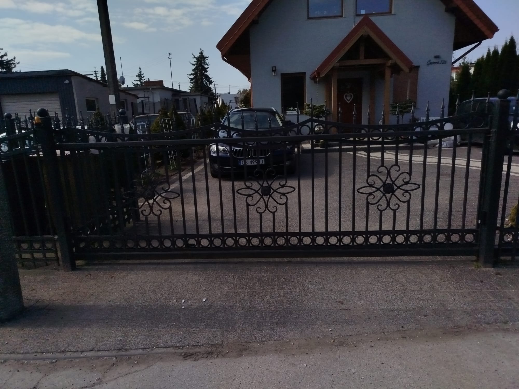 Kuta brama wjazdowa z dekoracyjnymi elementami na posesji w Bydgoszczy. W tle widoczny dom i zaparkowany samochód, co podkreśla funkcjonalność bramy.