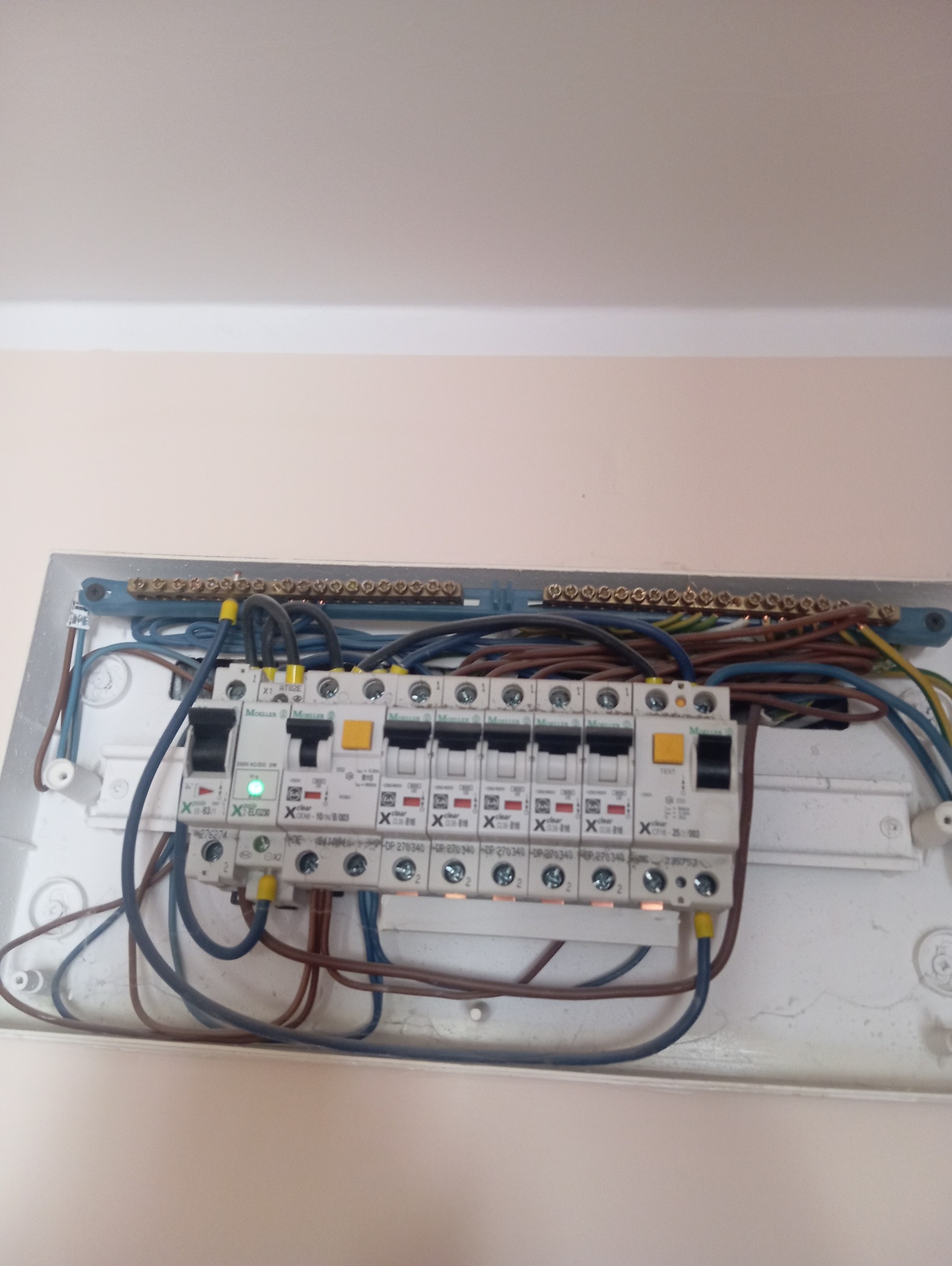 Rozdzielnica elektryczna z zainstalowanymi bezpiecznikami i podłączonymi przewodami. Widoczne listwy zaciskowe i oznaczenia na urządzeniach.