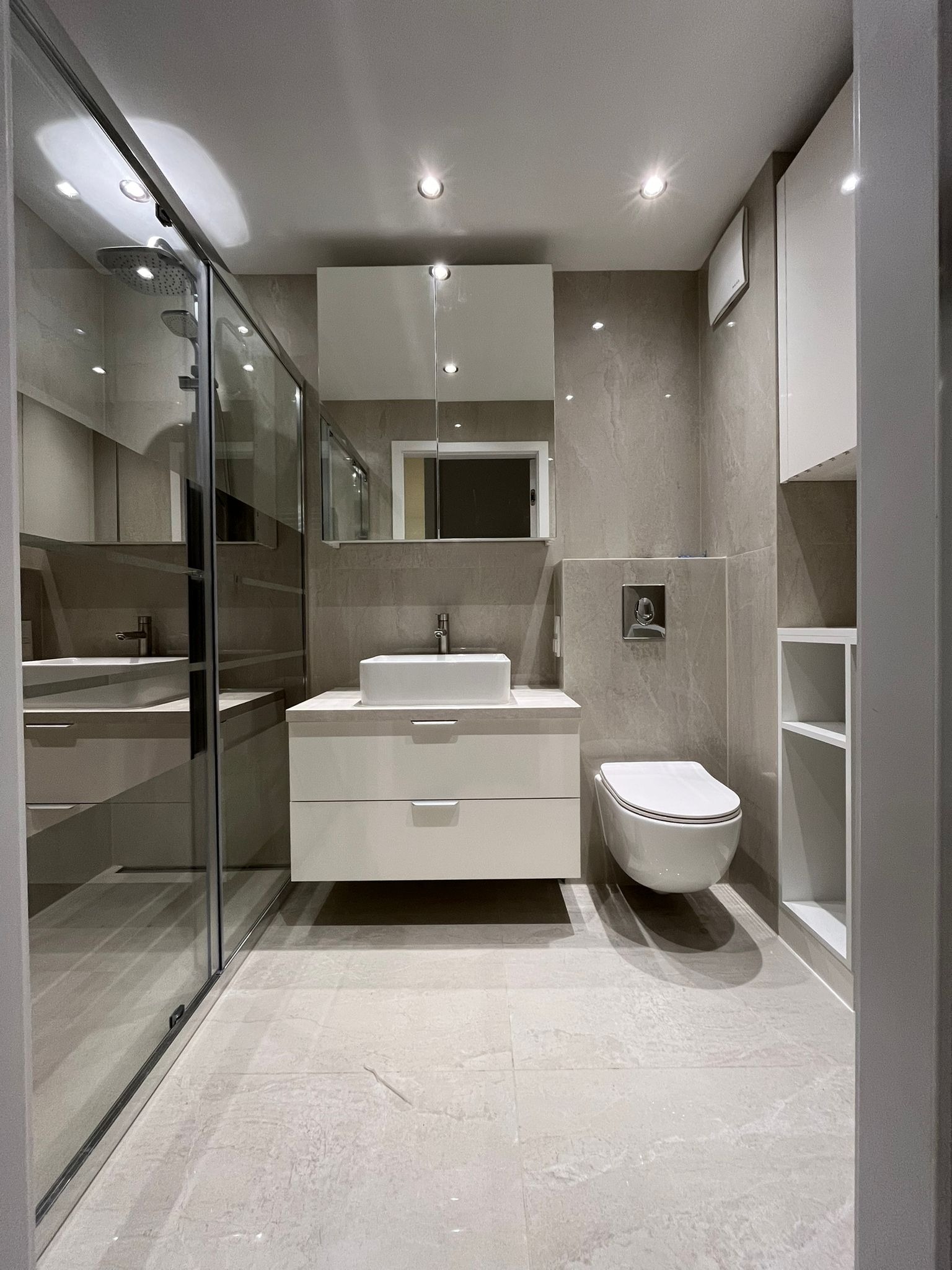 Nowoczesna łazienka w jasnych szarościach z białą armaturą i szafką pod umywalkę. Kabina prysznicowa ze szklanymi drzwiami. Minimalistyczny design.