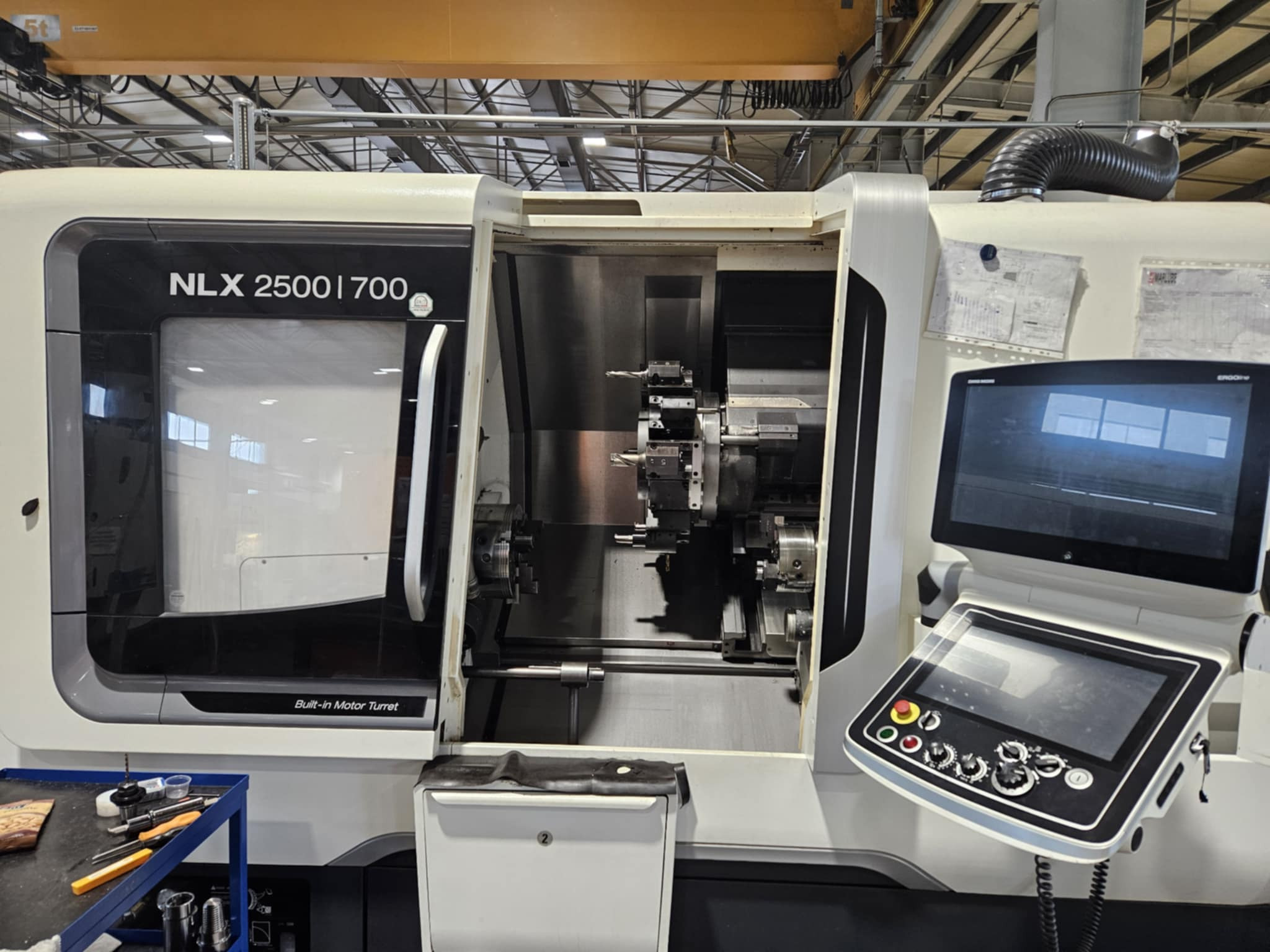 Nowoczesna tokarka CNC NLX 2500|700 z otwartą obudową, widoczne narzędzia i panel sterowania. W tle konstrukcja hali.