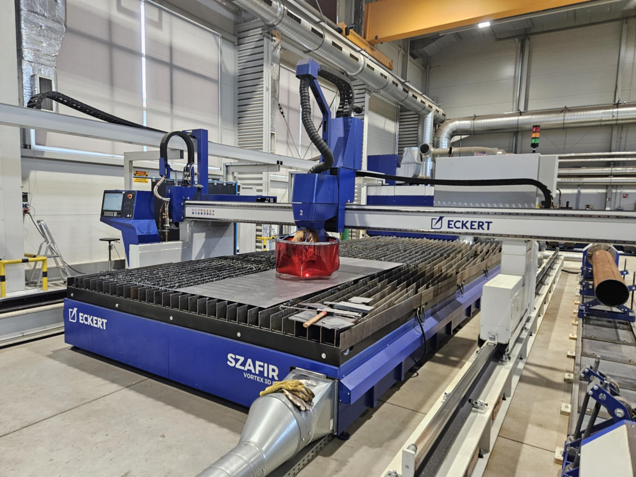 Szczegółowe ujęcie maszyny Eckert Szafir Vortex 3D do cięcia plazmowego blach, z czerwonym filtrem ochronnym nad obrabianym elementem. Widoczne rury wentylacyjne w tle.