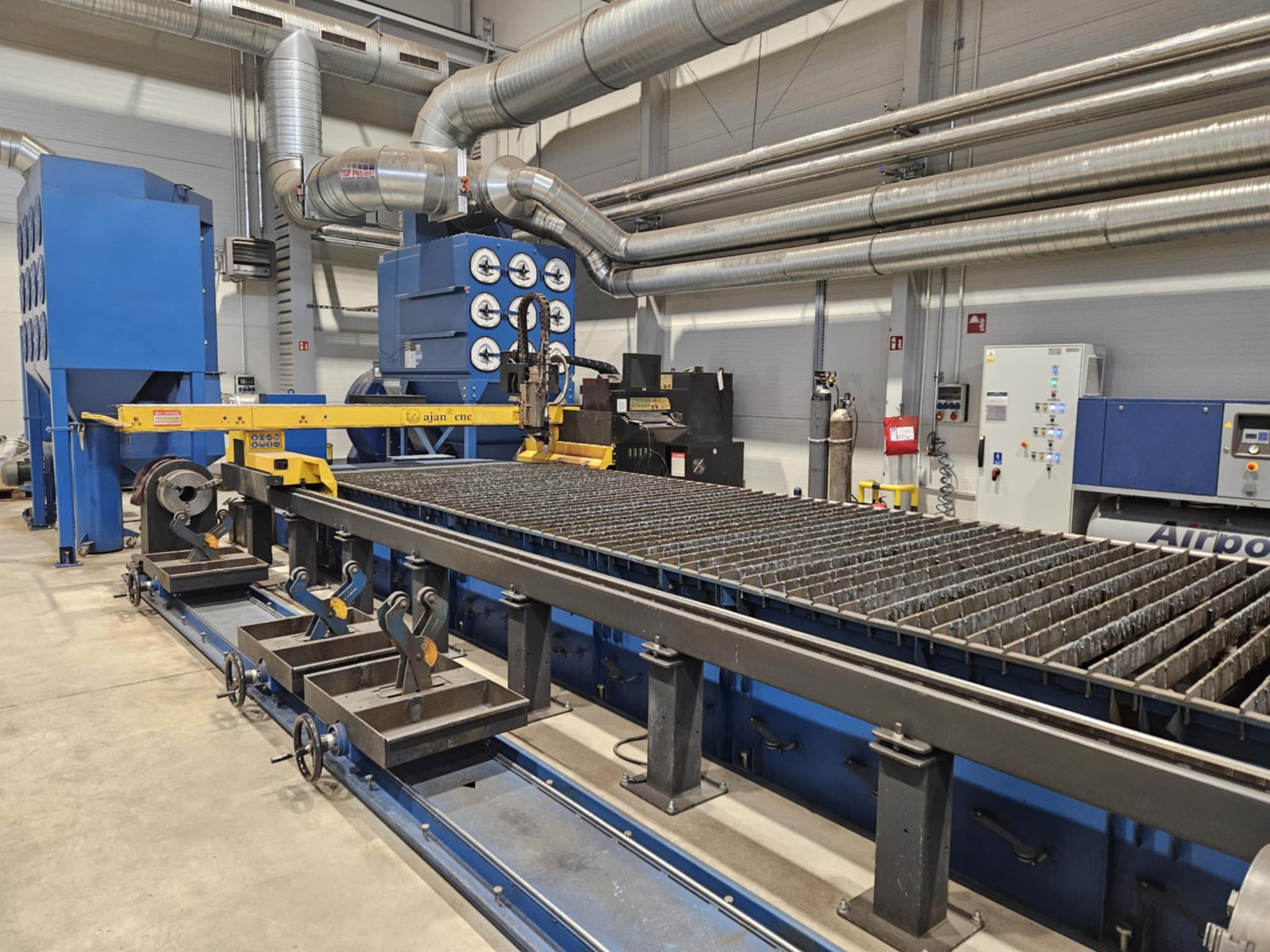 Plasma CNC: precyzyjne cięcie metalu na stole z rusztem, system odciągowy, przemysłowy design, detale obróbki skrawaniem.