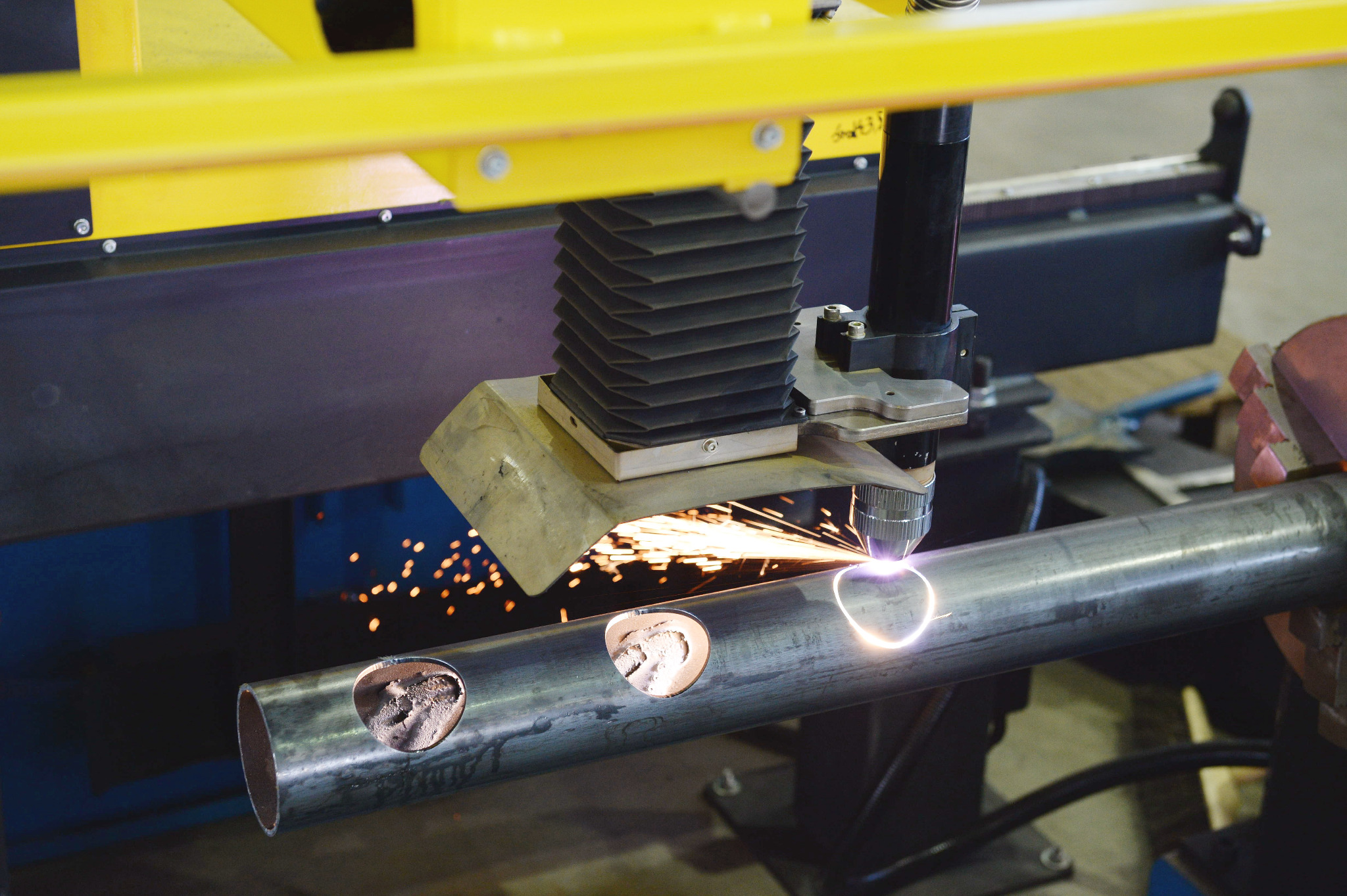Automatyczne cięcie plazmowe rury stalowej z trzema wyciętymi otworami. Iskry i jasne światło w miejscu cięcia. Żółta rama maszyny. Obróbka CNC.