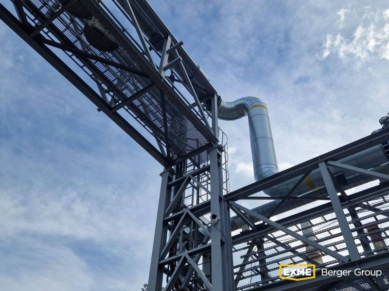 Metalowa konstrukcja wsporcza z rurociągami na tle błękitnego nieba. Widok z dołu, podkreślający złożoność konstrukcji i inżynieryjny charakter.