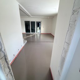 ProFoundation - Wnętrze w trakcie wylewki samopoziomującej, widoczne ściany w stanie surowym i przygotowane podłoże. Czerwona taśma oddziela wylewkę od ścian.