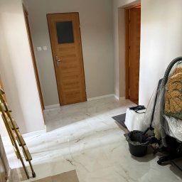 Vladyslav Krasovskyi ProFundation - Jasne wnętrze po remoncie: białe marmurowe płytki podłogowe, świeżo pomalowane ściany w odcieniach beżu, drewniane drzwi z szybą. Widoczna drabina i sprzęt sprzątający.