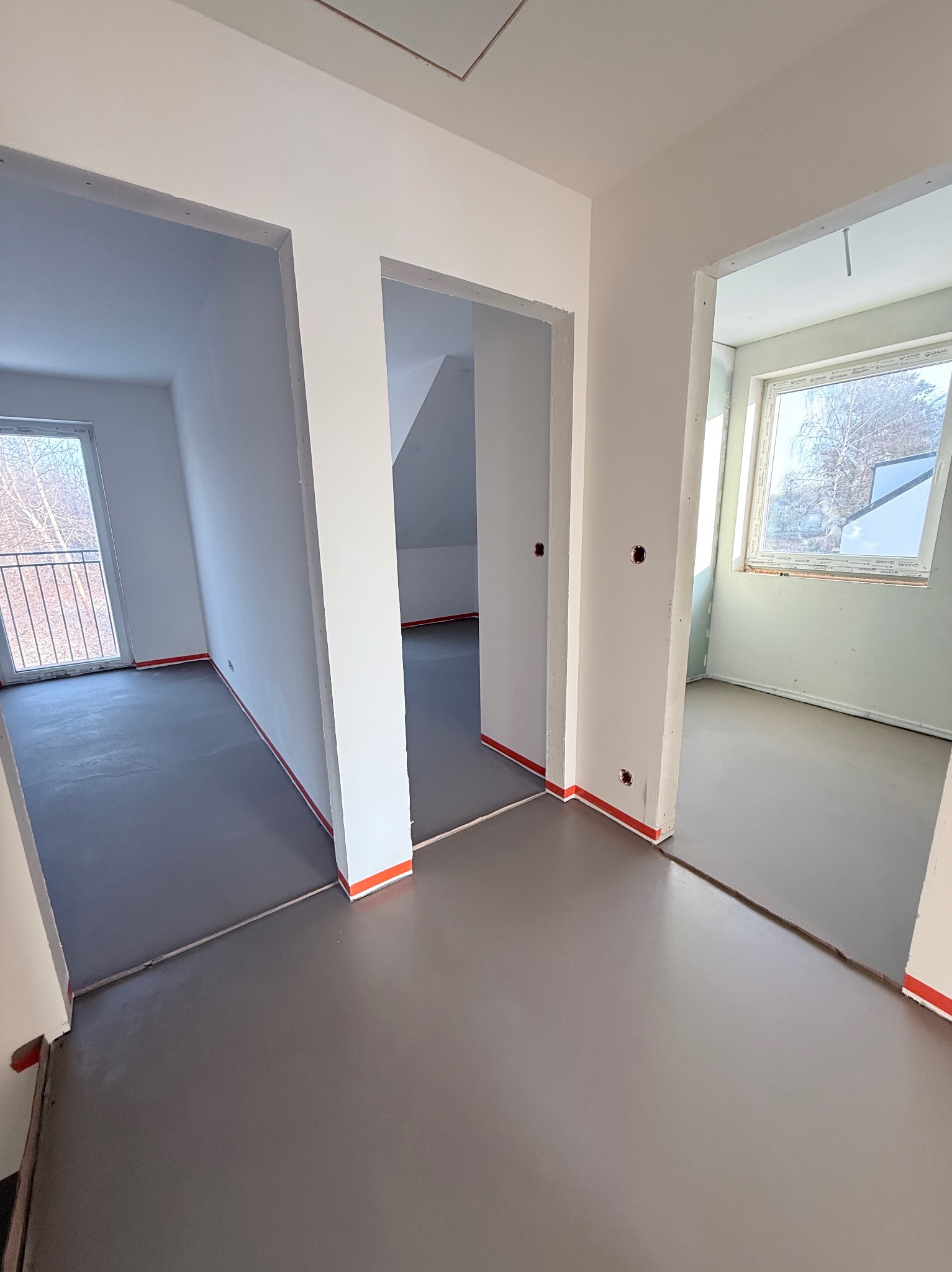 Wnętrze po wylaniu samopoziomującej wylewki, widoczne przejścia między pomieszczeniami, zabezpieczone ściany taśmą. Szary kolor wylewki, surowy stan wykończenia.