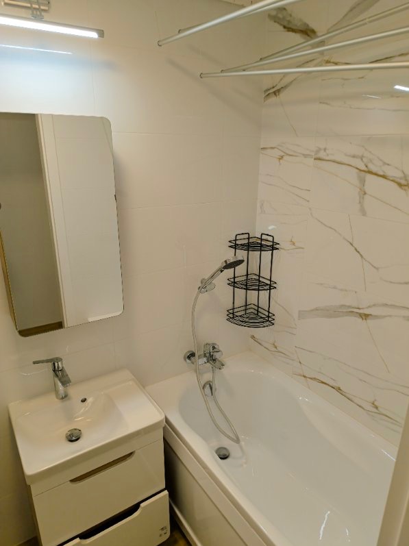 Biała łazienka z wanną, umywalką z szafką i lustrem. Na ścianie płytki imitujące marmur z złotymi żyłami. Suszarka sufitowa. Minimalistyczny design.