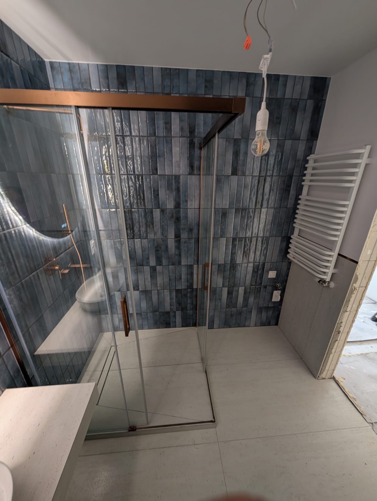 Nowoczesna łazienka z kabiną prysznicową typu walk-in, wykończona w odcieniach granatu i bieli. Widoczny grzejnik drabinkowy i oświetlenie.