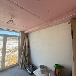 FINALITO - Wykończenia i Budownictwo Oskar Bożys - Wnętrze w trakcie prac wykończeniowych: sufit z płyt karton-gips w kolorze różowym, ściany przygotowane do malowania, widoczne narzędzia i materiały budowlane.