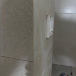 FINALITO - Wykończenia i Budownictwo Oskar Bożys - Beżowe płytki ścienne z fugami, narożnik i gniazdka elektryczne w łazience w trakcie remontu. Widoczny fragment podłogi z odpływem.