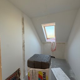 FINALITO - Wykończenia i Budownictwo Oskar Bożys - Poddasze w trakcie prac wykończeniowych: ocieplenie, instalacja ogrzewania podłogowego, okno dachowe zabezpieczone folią. Widoczne materiały izolacyjne.