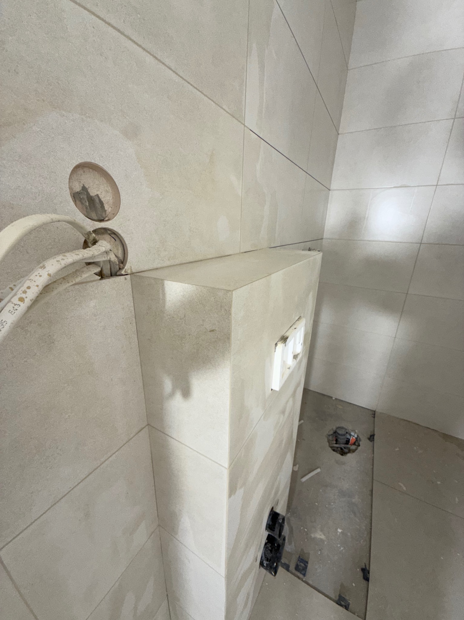 Wykończona łazienka w trakcie prac: ułożone płytki na ścianach i podłodze, widoczne rury i instalacja podtynkowa WC. Minimalistyczny design w jasnych odcieniach.