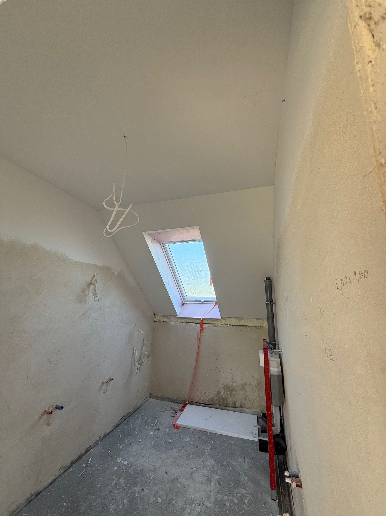 Pokój na poddaszu w trakcie prac wykończeniowych: surowe ściany z instalacjami, okno dachowe i widoczne przewody elektryczne. Przygotowanie do dalszych prac.